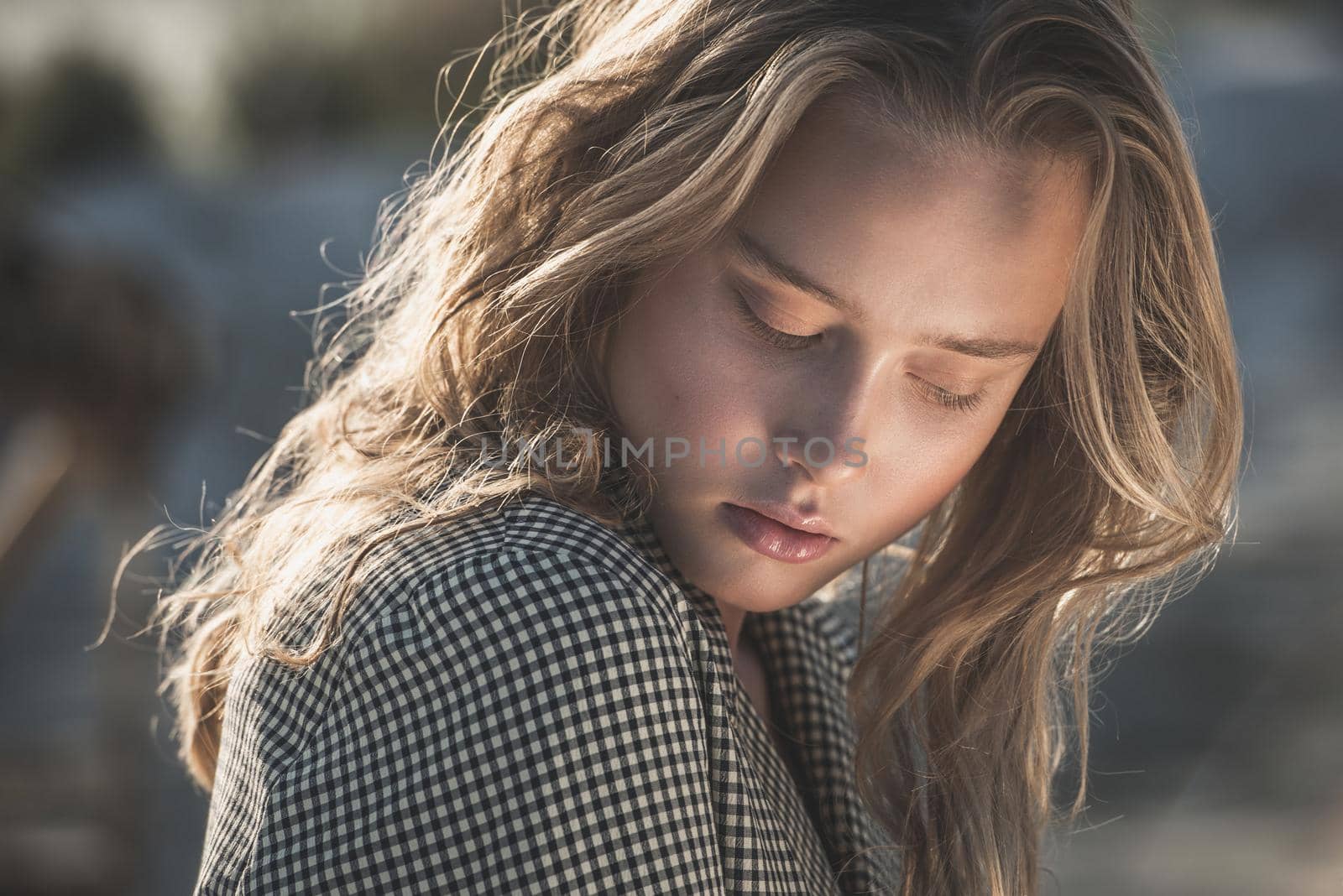 Debonair blonde girl sitting at sandy beach in autumn sunset. Outdoor portrait of pretty curly fashionable girl