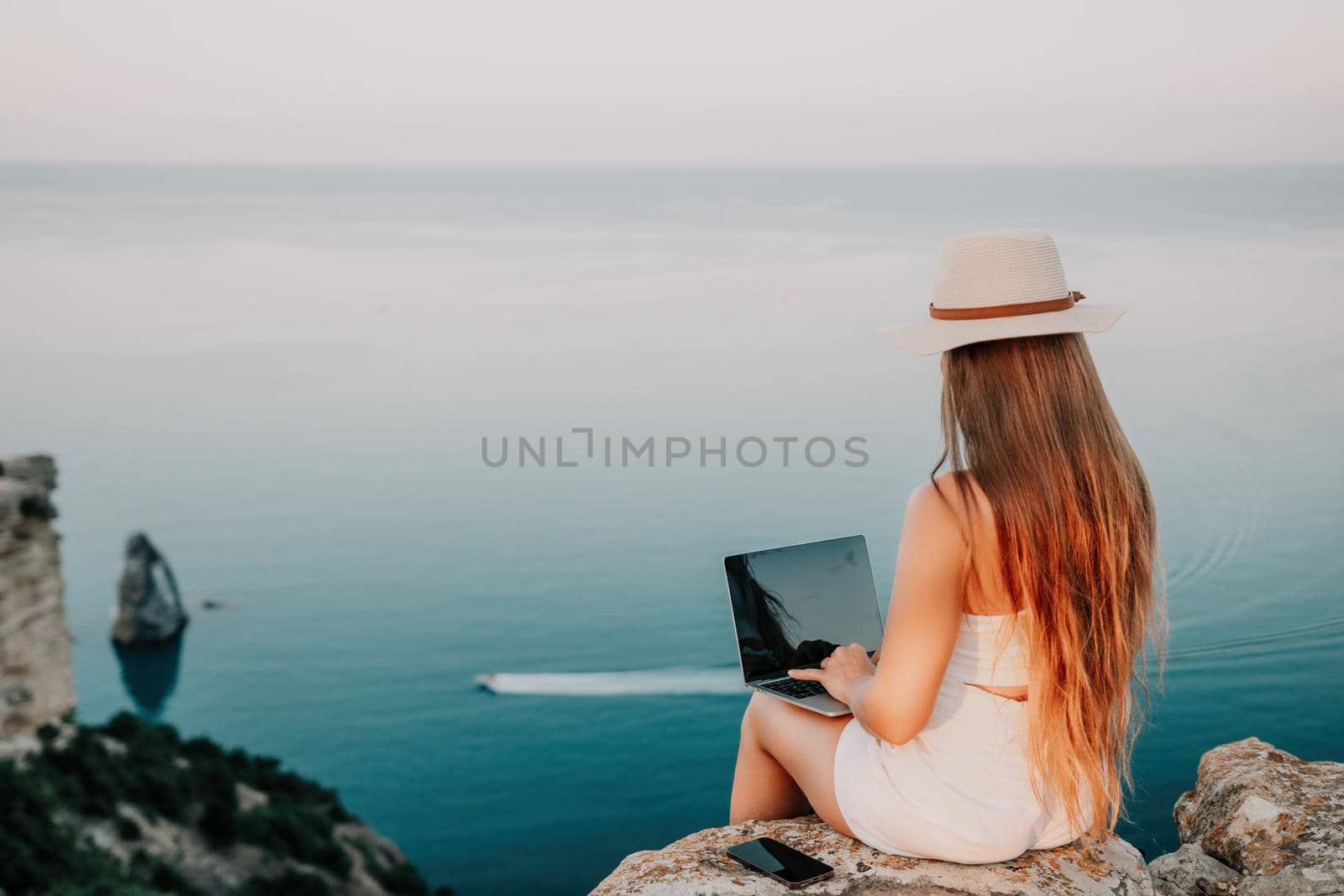 Digital nomad, Business woman working on laptop by the sea. Pretty lady typing on computer by the sea at sunset, makes a business transaction online from a distance. Freelance, remote work on vacation by panophotograph