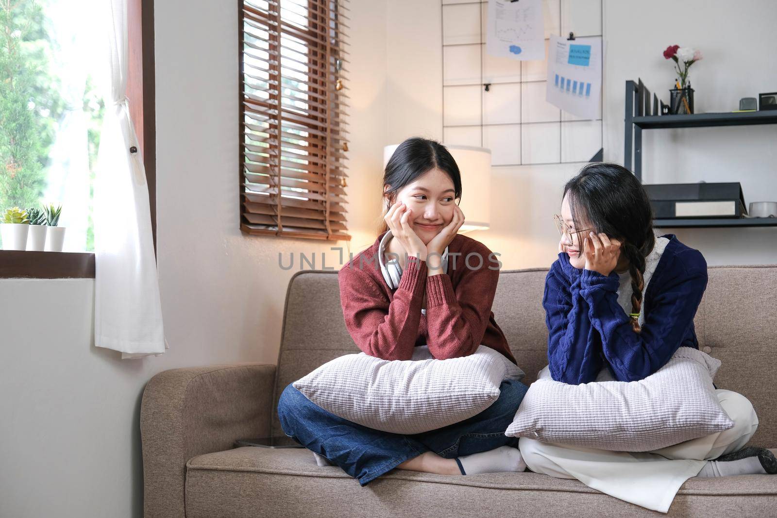 Happy asian female friends at home sitting on couch. two young women with chatting on sofa gossiping and sharing secrets discussing life and relations. Friendship trust concept.