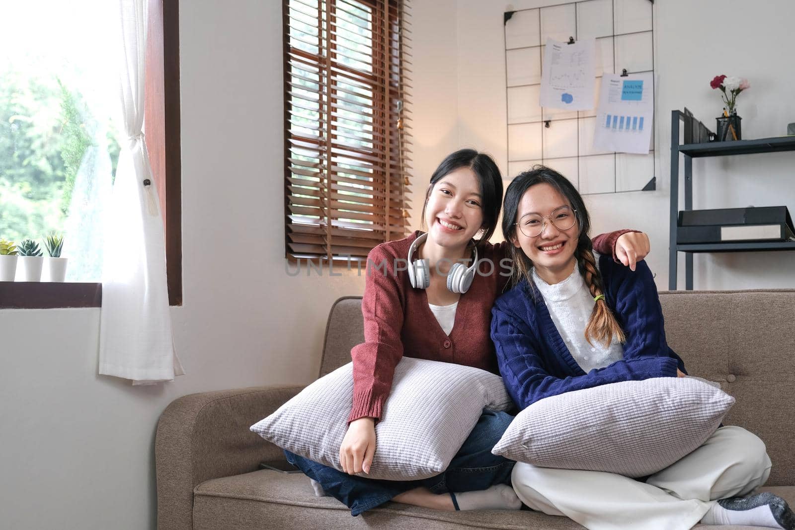 Asian beautiful lesbian women couple hugging girlfriend in living room. Attractive two female gay friend sitting on sofa in living room, feel happy and enjoy spending time together on holiday in house.