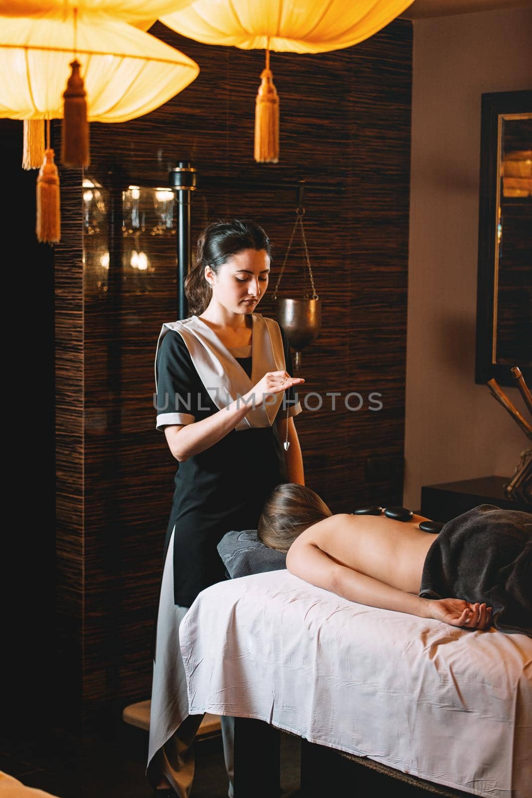 Young charming girl on a panchakarma procedure laying on a massage table. beautiful woman spending time at modern spa cabinet relaxing. Soft yellow light by Ashtray25
