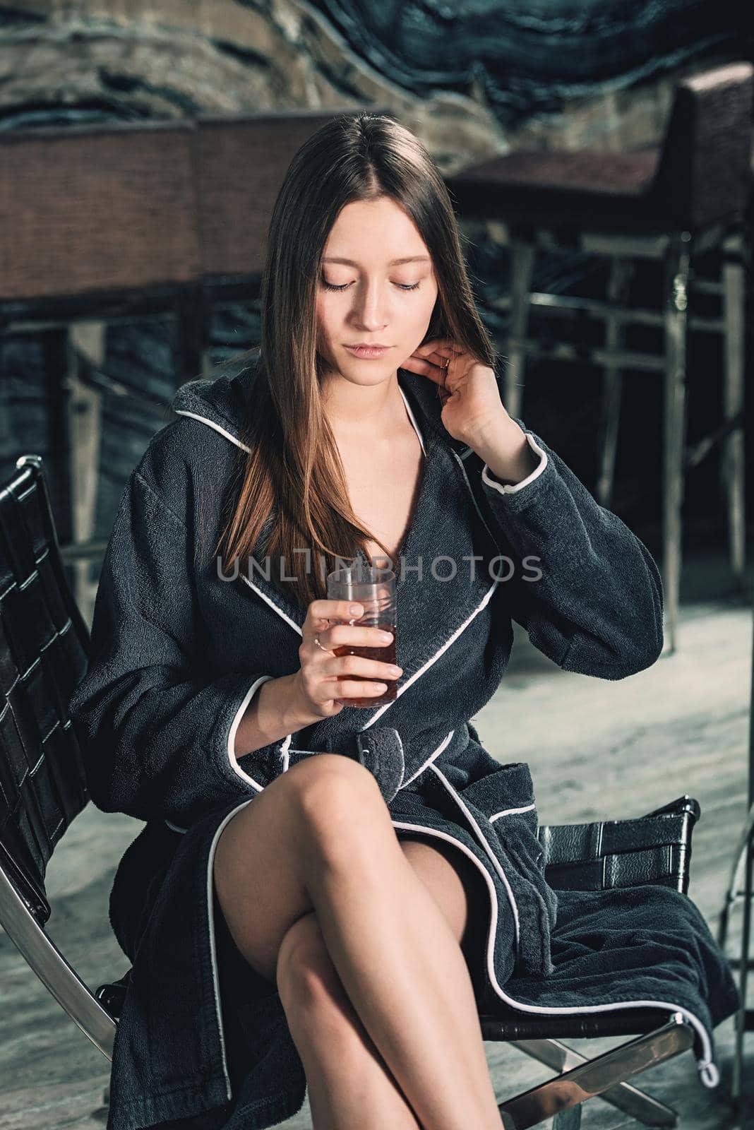 Portrait of young beautiful woman relaxing in a chair in a bathrobe with a detox drink in a hand. Luxery spa center