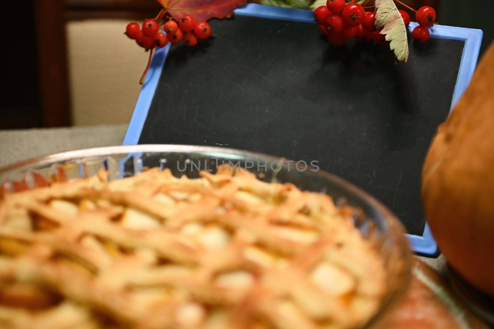 Selective focus. Branch of viburnum berries hanging on a chalkboard with copy space for promotional text, red autumn maple leaves, a sweet homemade classic American pumpkin apple pie with crispy crust