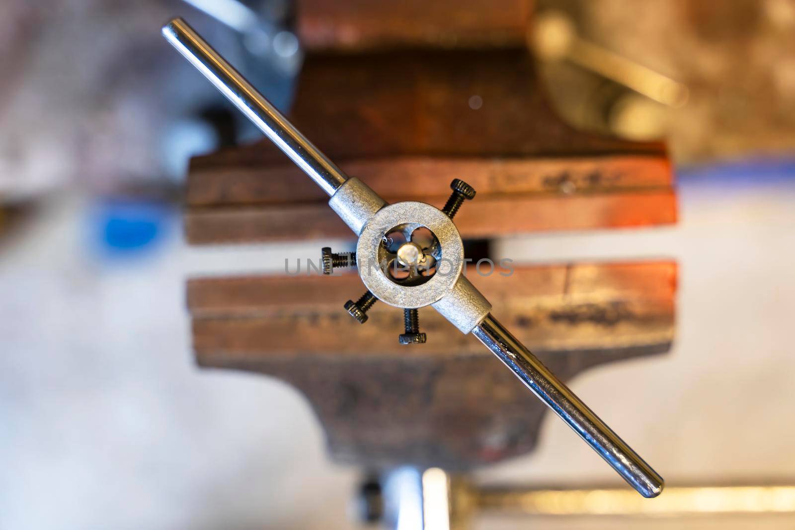 threading on a part clamped in an old iron vise in the workshop. Repair of equipment in the garage. die holder. auto repair shop and motorcycle workshop