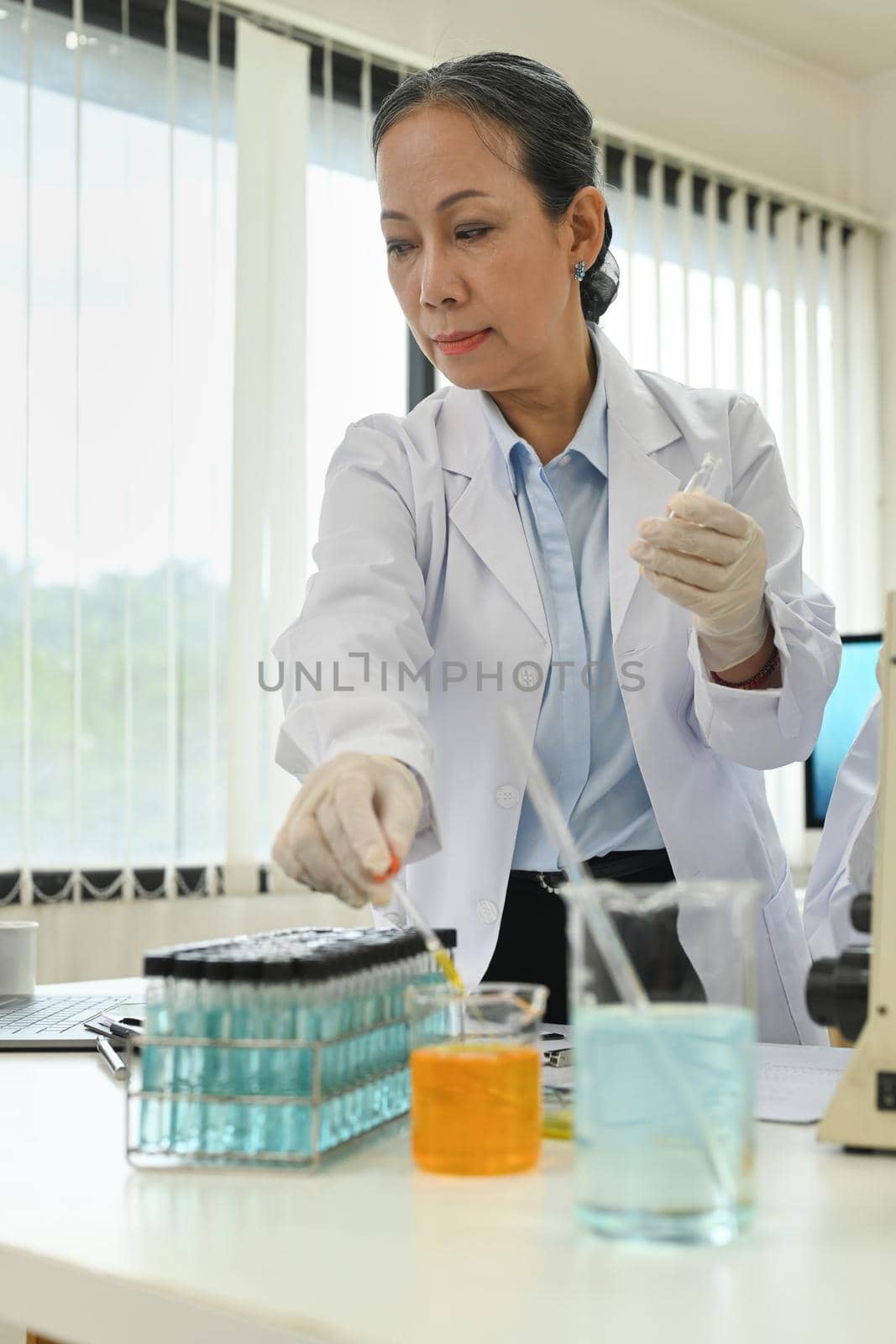 Middle age female scientist preparing and conducting experiment in laboratory. Concepts of medicine and science researching.