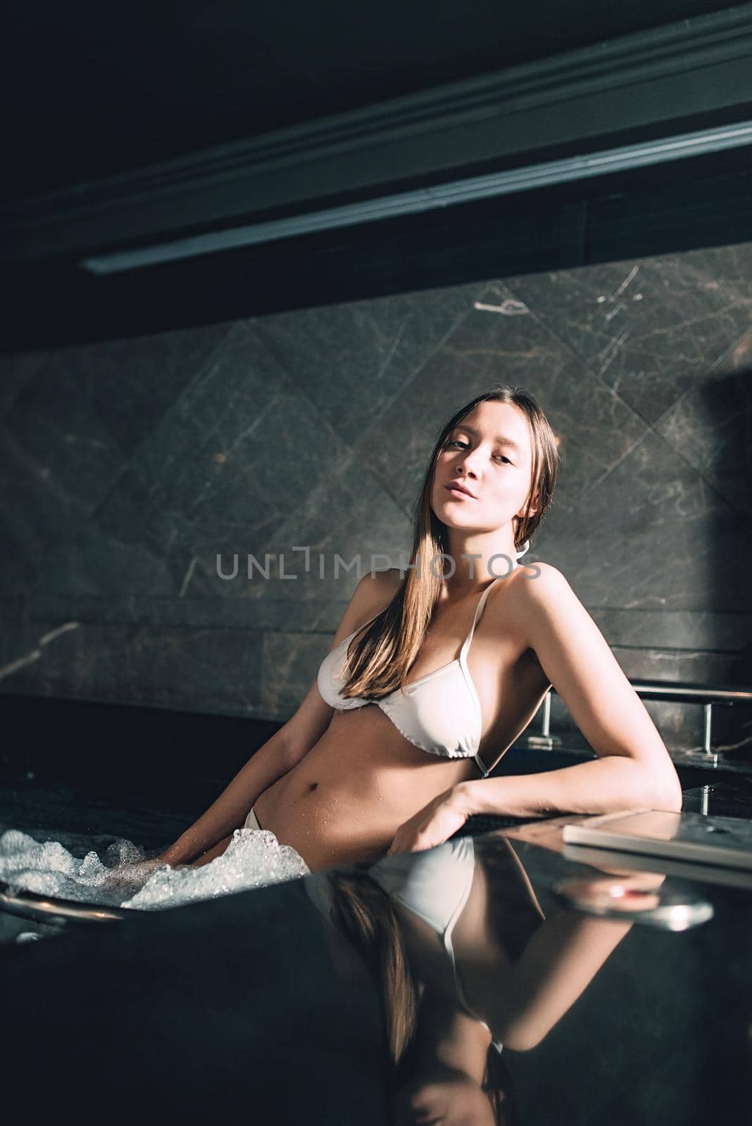 Sexy beautiful caucasian woman relaxing in a pool with jacuzzi. Dark room. Poor lighting.