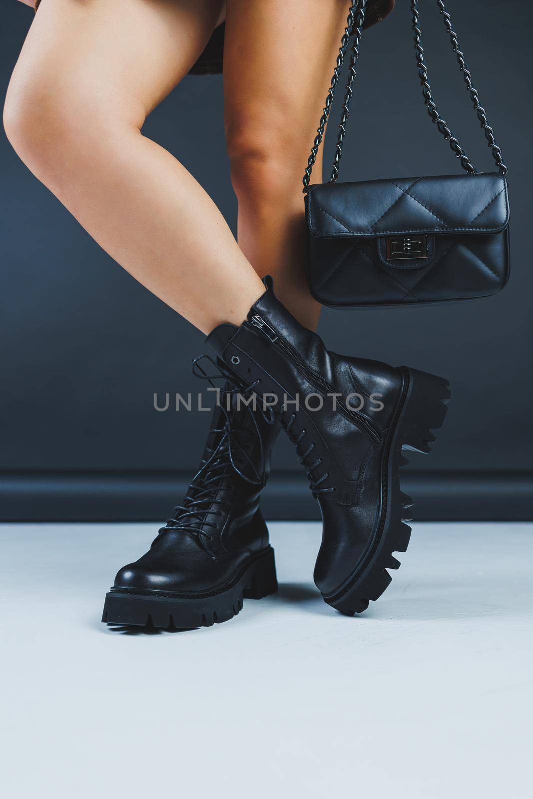 Close-up of female legs in black leather lace-up shoes. Black leather handbag in female hands. New autumn collection of women's leather shoes 2022