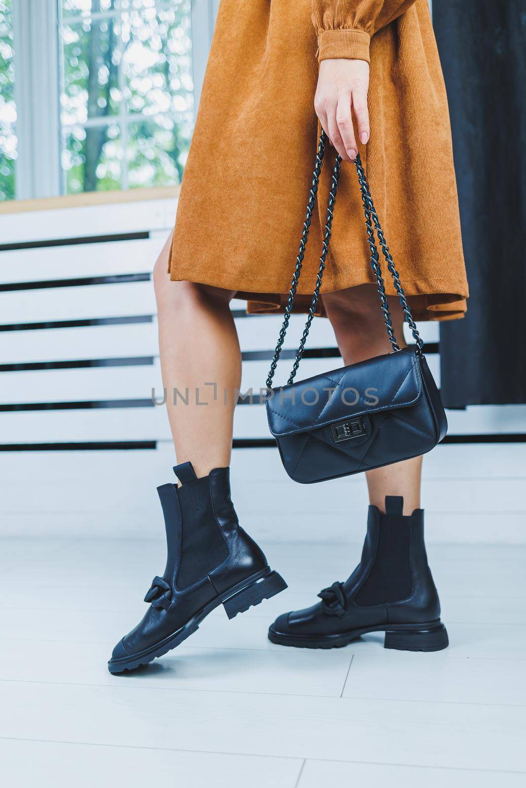 Close-up of female legs in black leather lace-up shoes. Black leather handbag in female hands. New autumn collection of women's leather shoes 2022