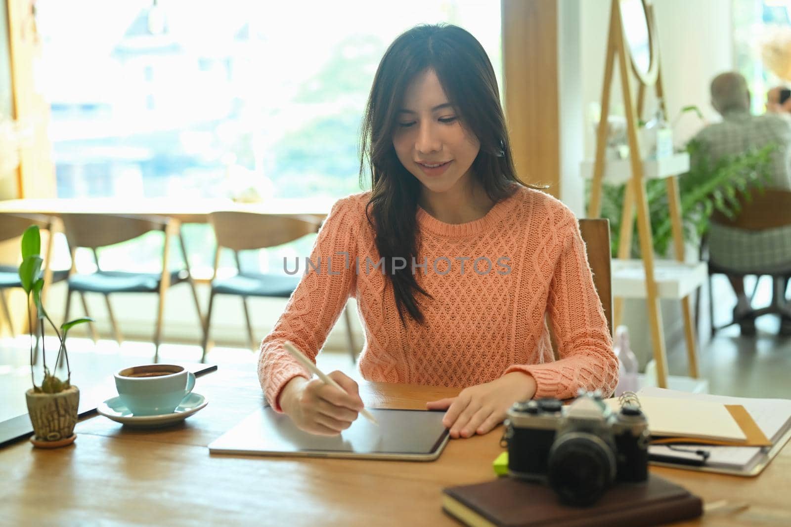 Young woman in warm clothes working with digital tablet in modern coffee shop.