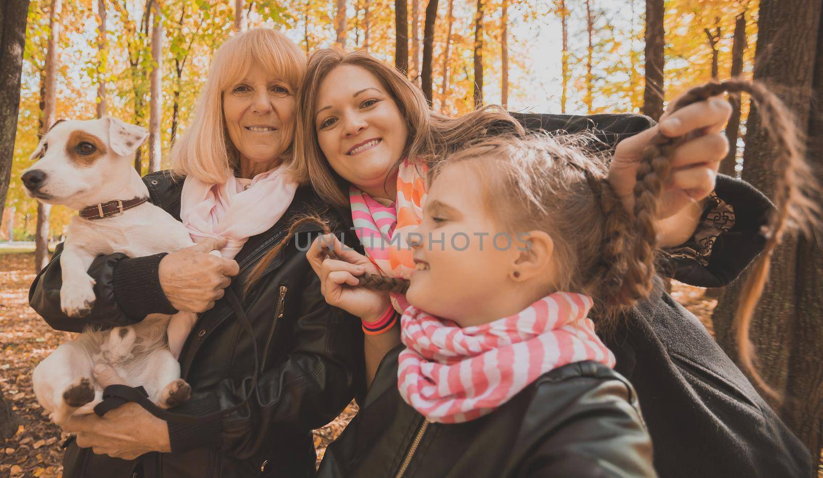 Mother, grandmother and little granddaughter with jack russell terrier dog taking selfie by smartphone outdoors in autumn nature. Family, pets and generation concept.