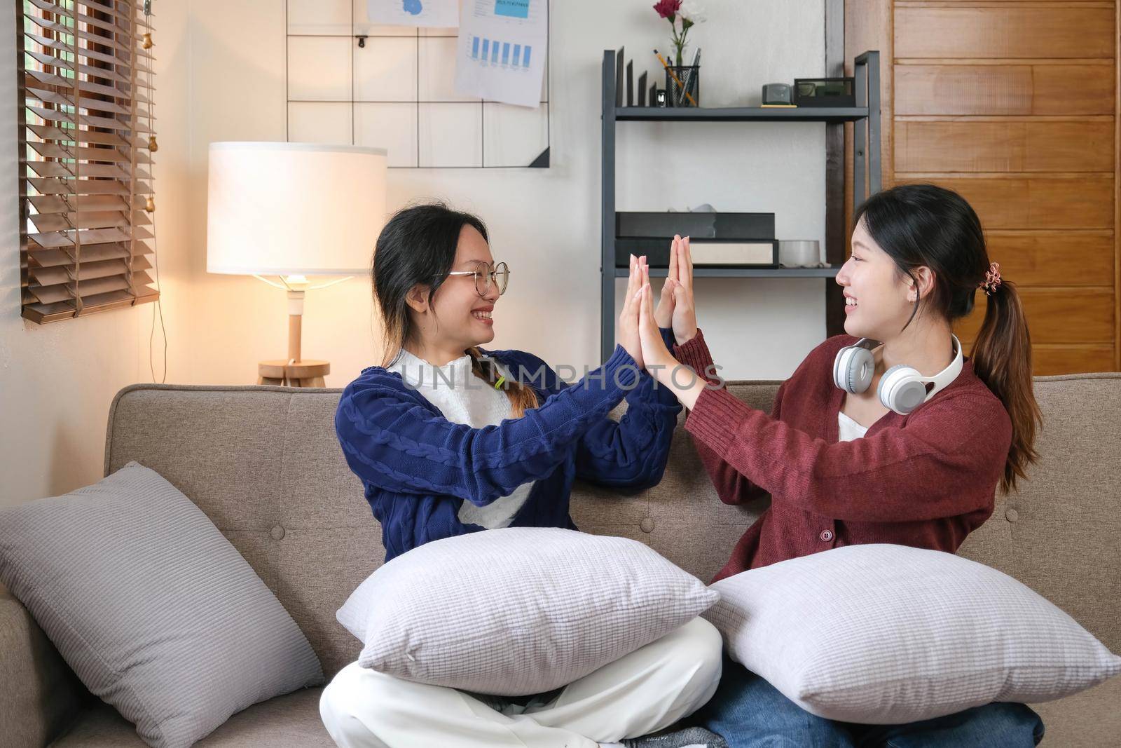 Two Young woman cheering together for sport on TV in cozy living room at home. by wichayada