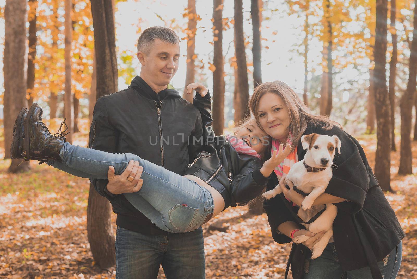 Family spend time in autumn park with a dog. Father, mother and daughter and jack russell terrier dog having fun in fall by Satura86