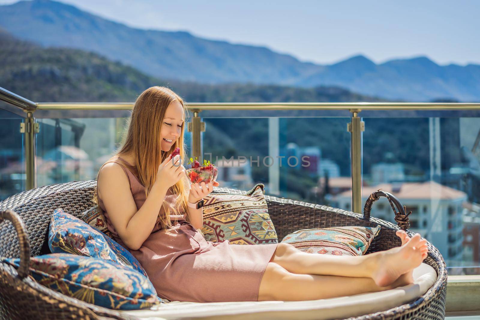 Portrait of gorgeous woman wearing beautiful dress sitting in a patio and eating strawberry.