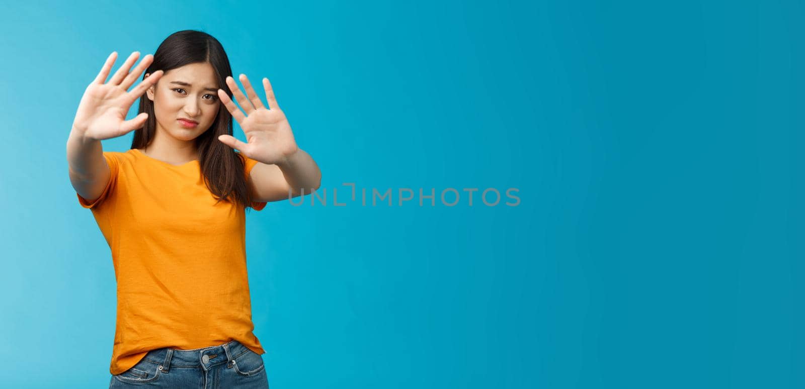 Asian moody displeased silly timid girl asking turn off light not photograph her, raise hands block, cover face step back and cringe disappointed, standing blue background upset reluctant by Benzoix