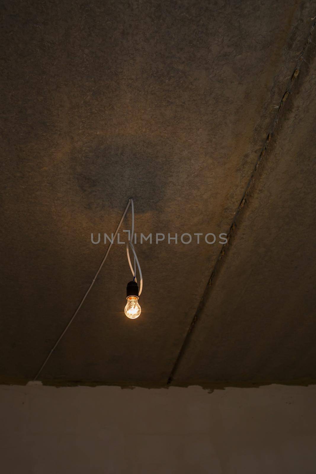 Light bulb on the ceiling. Lonely light bulb and wire sticking out of the ceiling during a repair by Dmitrytph