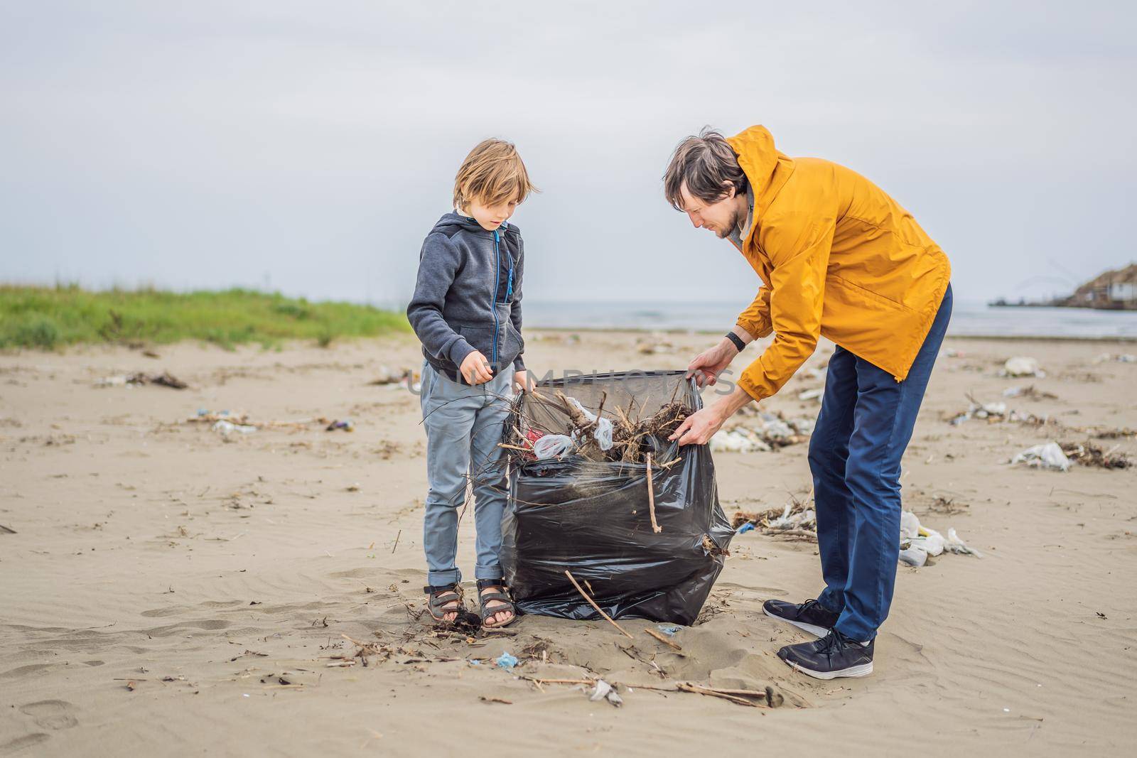 Dad and son in gloves cleaning up the beach pick up plastic bags that pollute sea. Natural education of children. Problem of spilled rubbish trash garbage on the beach sand caused by man-made by galitskaya