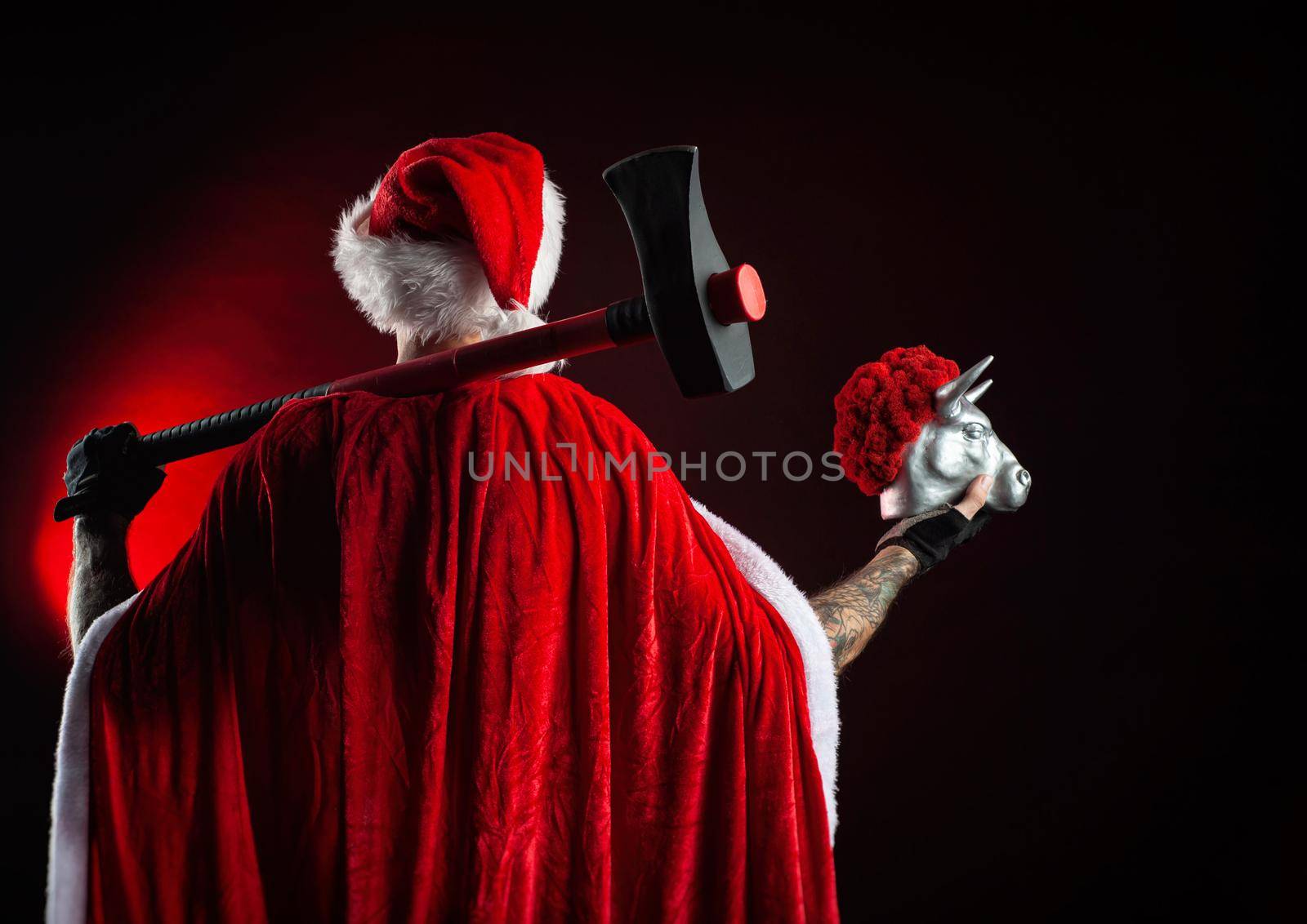 a man in a red Santa Claus Cape with an axe and a metal bull figurine symbol of the new year 2021 by Rotozey