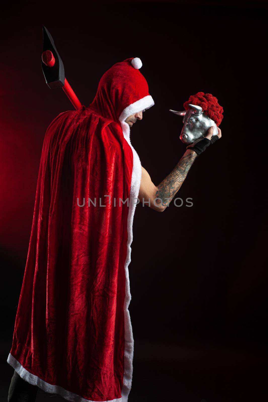 a man in a red Santa Claus Cape with an axe and a metal bull figurine symbol of the new year 2021 by Rotozey
