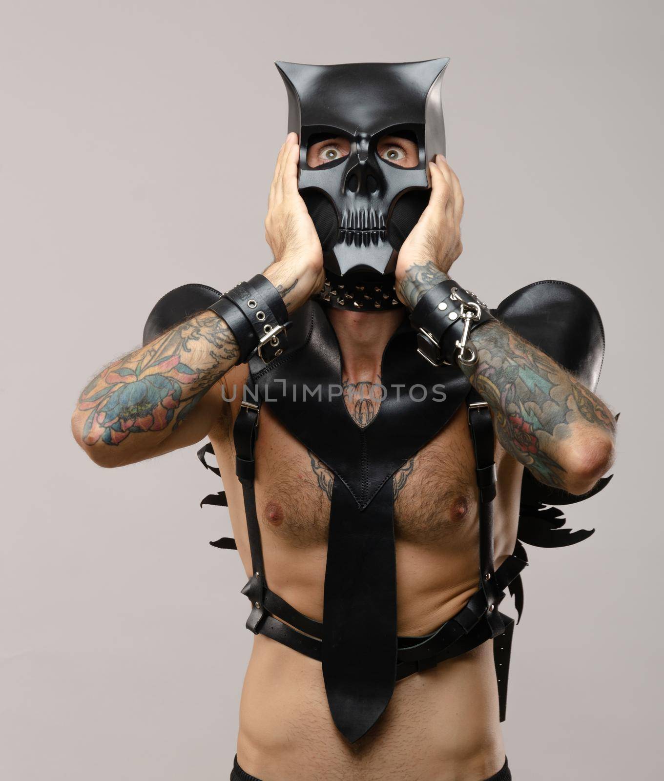 the man in a bdsm mask of a demon-skull, dressed in leather with leather bracelets and belts