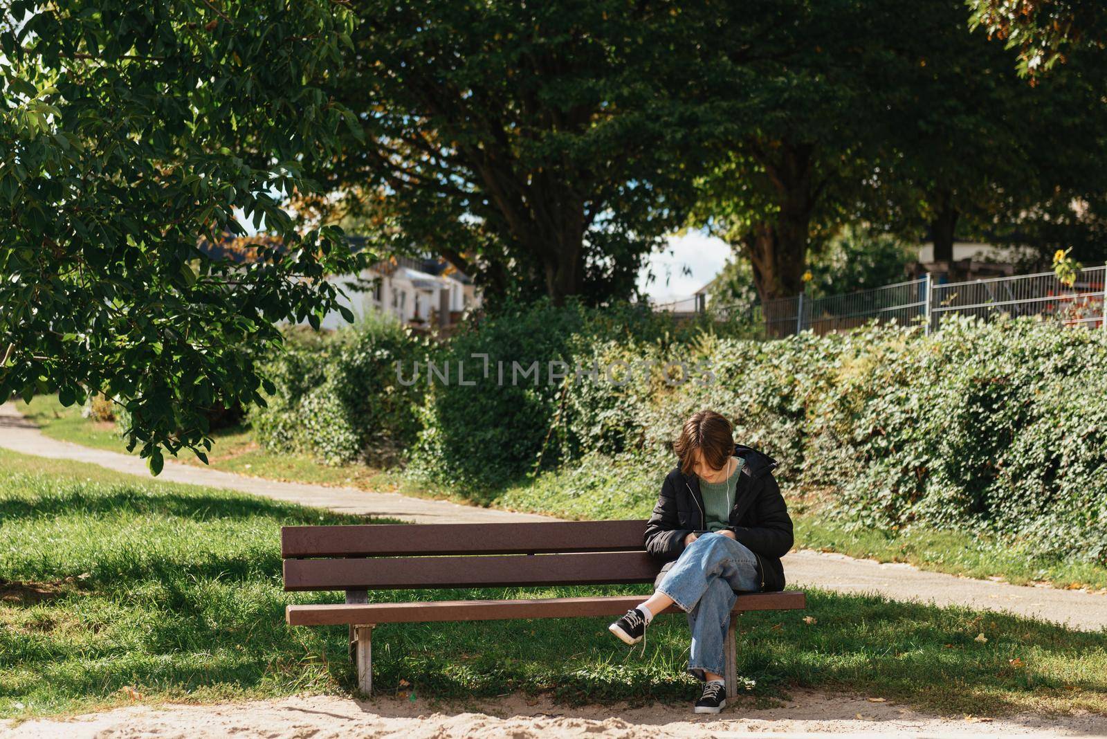 Happy girl using a smart phone in street sitting on a bench. Beautiful girl sitting on a bench, fashion life style with your phone writes a message on social networks, sunny day in the park, relaxing, after work business woman. by Andrii_Ko