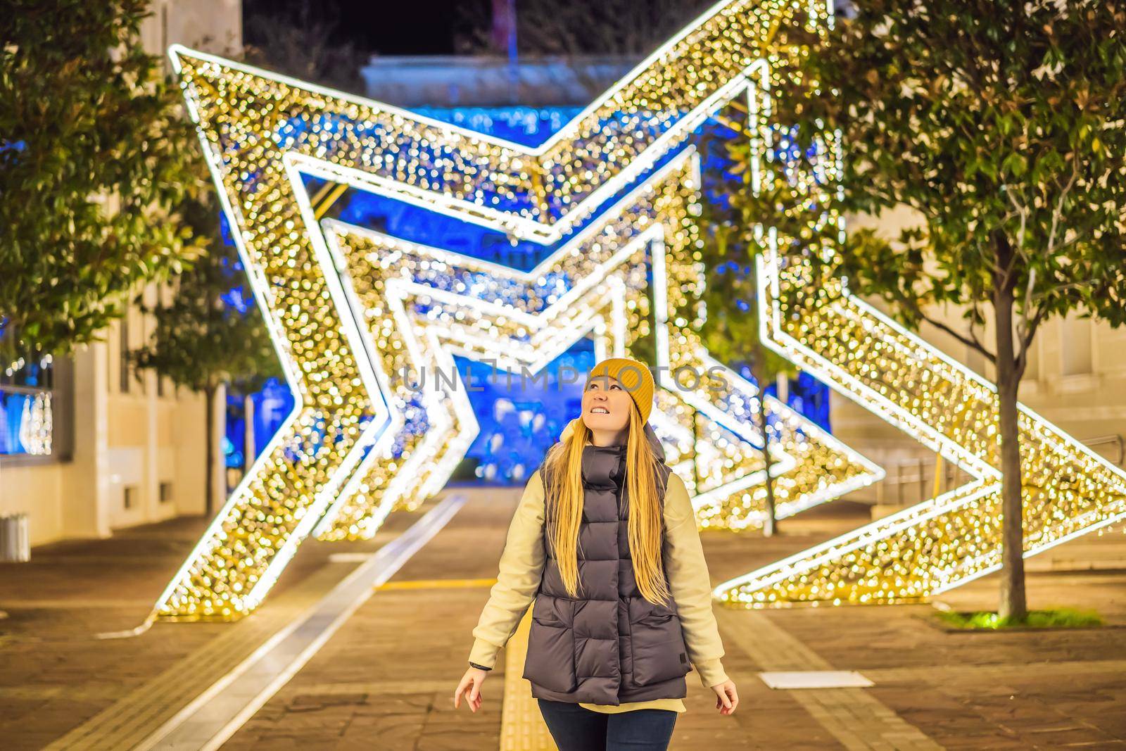 Girl walking in Christmas traditional market decorated with holiday lights in the evening. Winter portrait beautiful young woman outdoors in front of Xmas holidays decorations.
