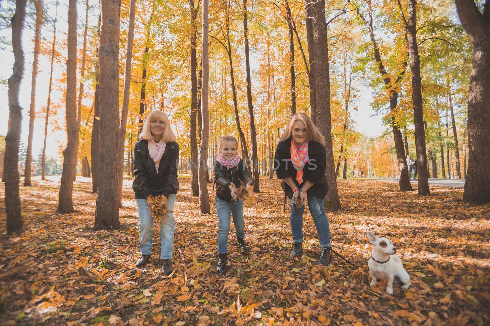 Grandmother and mother with granddaughter throw up fall leaves in autumn park and having fun. Generation, leisure and family concept. by Satura86