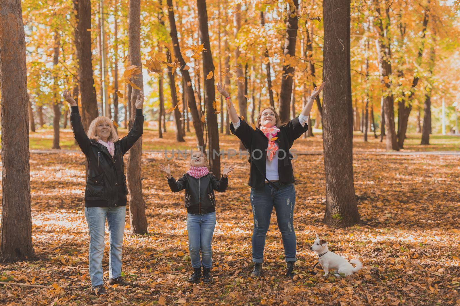 Grandmother and mother with granddaughter throw up fall leaves in autumn park and having fun. Generation, leisure and family concept