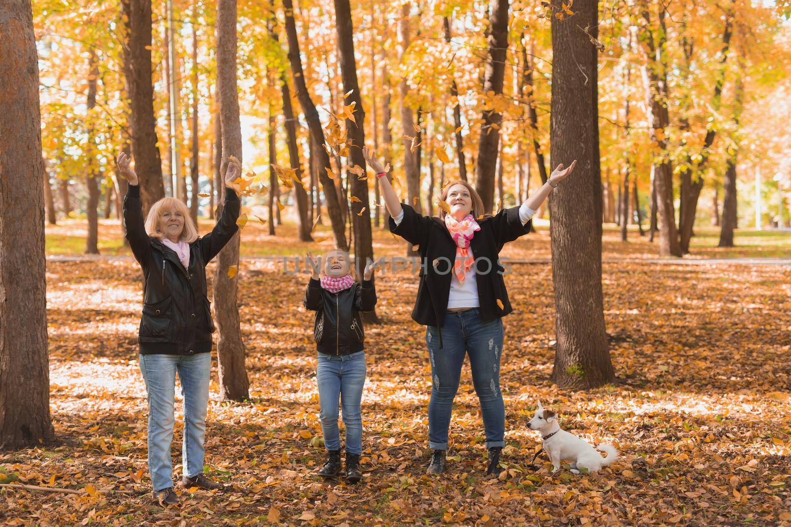 Grandmother and mother with granddaughter throw up fall leaves in autumn park and having fun. Generation, leisure and family concept. by Satura86