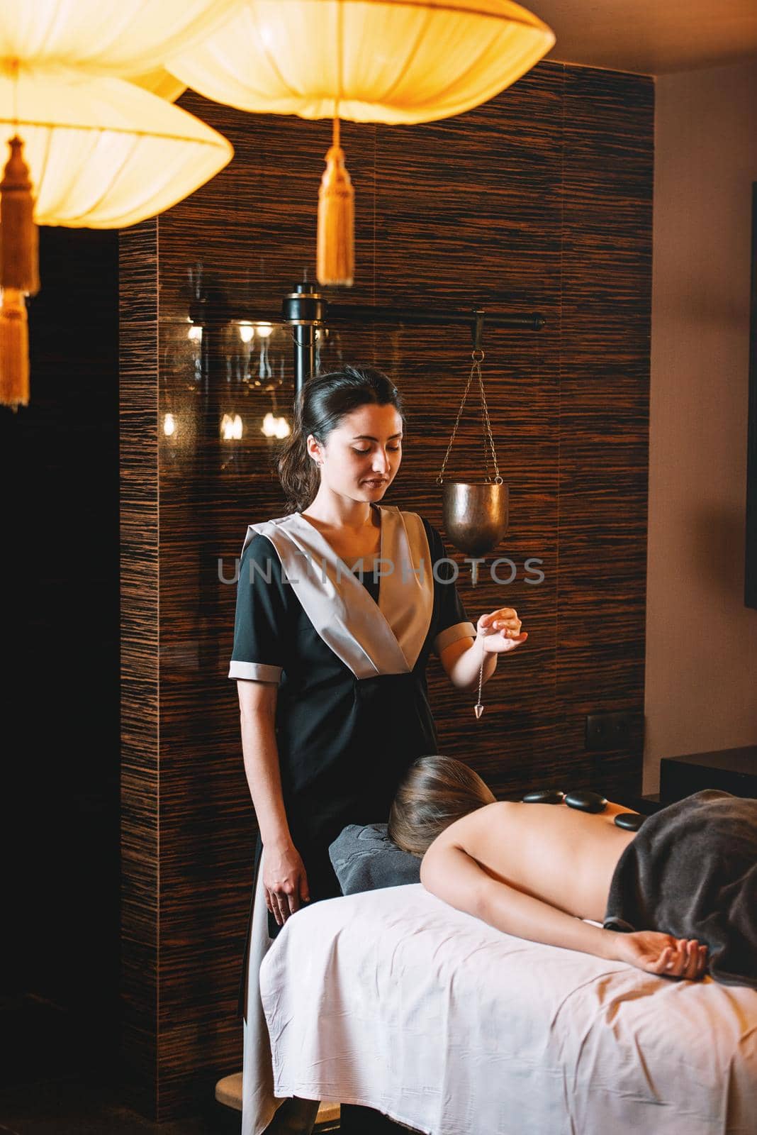 Young charming girl on a panchakarma procedure laying on a massage table. beautiful woman spending time at modern spa cabinet relaxing. Soft yellow light by Ashtray25