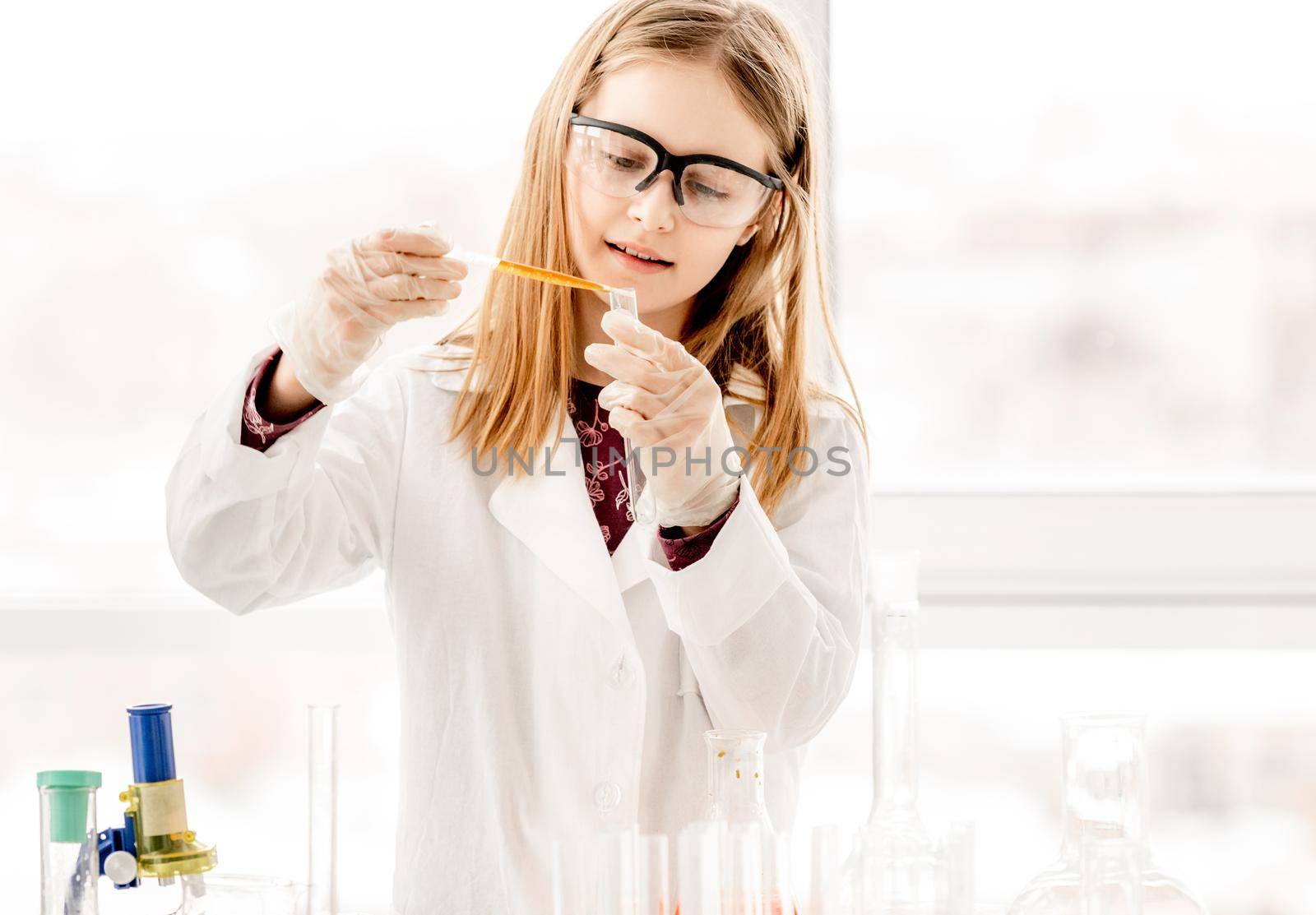 Girl doing scientific chemistry experiment wearing protection glasses and measuring liquid. Schoolgirl with test equipment on school lesson