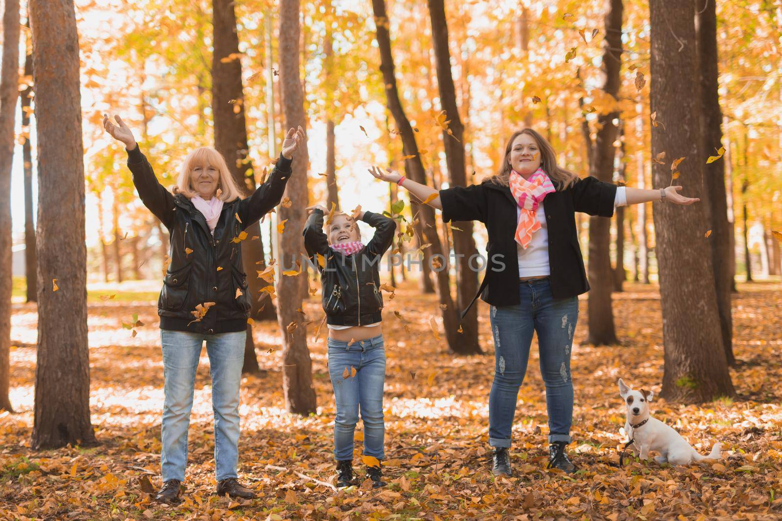 Grandmother and mother with granddaughter throw up fall leaves in autumn park and having fun. Generation, leisure and family concept