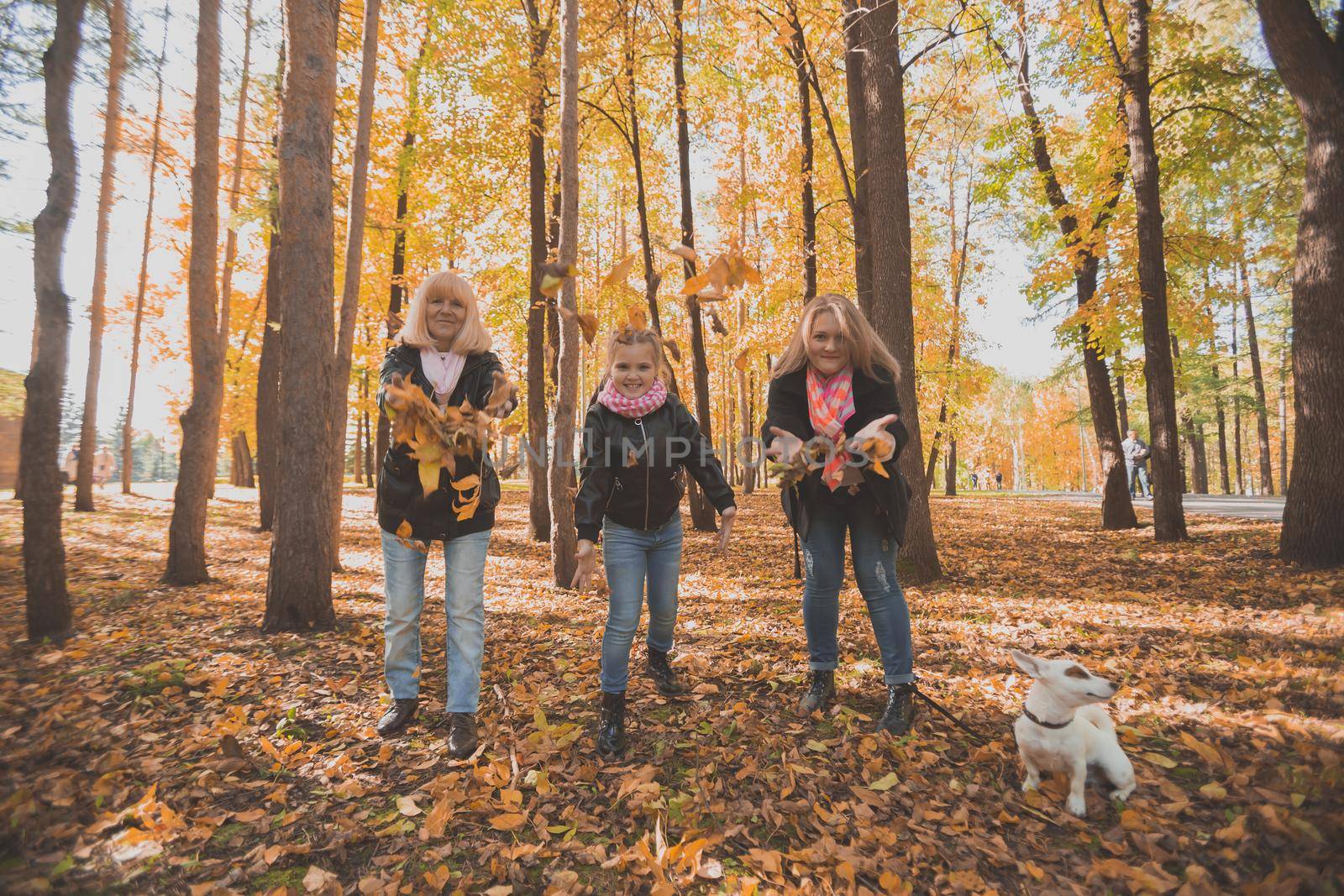 Grandmother and mother with granddaughter throw up fall leaves in autumn park and having fun. Generation, leisure and family concept