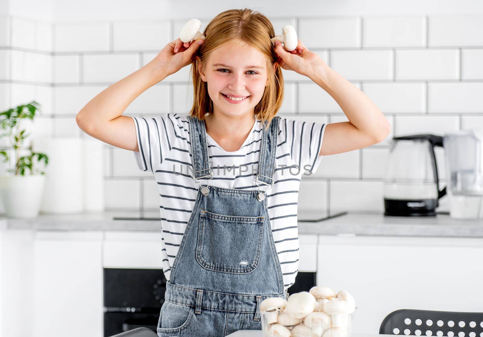 Preteen girl with champignons posing at kitchen and smiling. Pretty child with mushrooms food at home