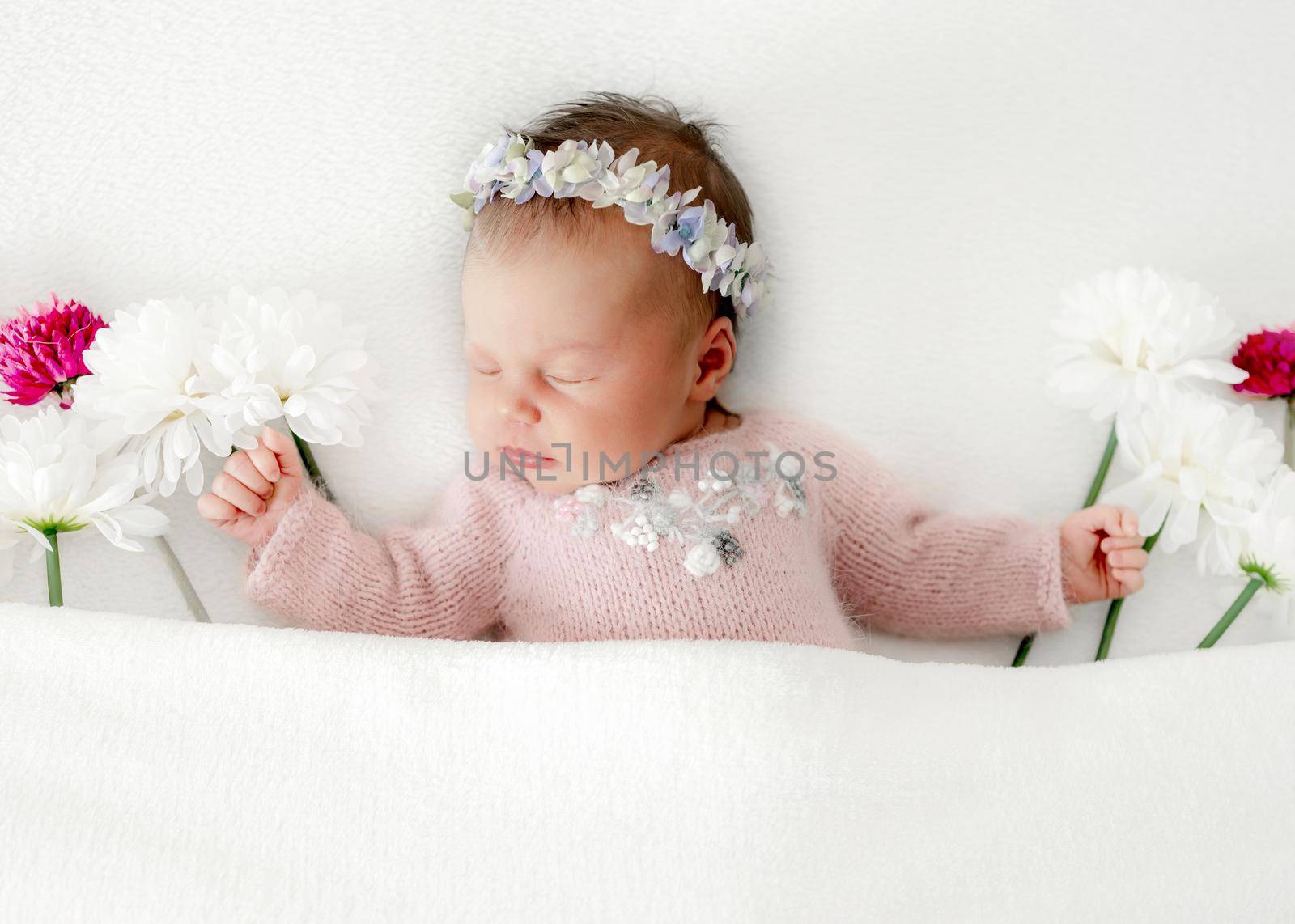 Newborn baby girl wearing wreath sleeping in bed decorated with white and pink flowers. Infant child kid spring blossom studio portrait