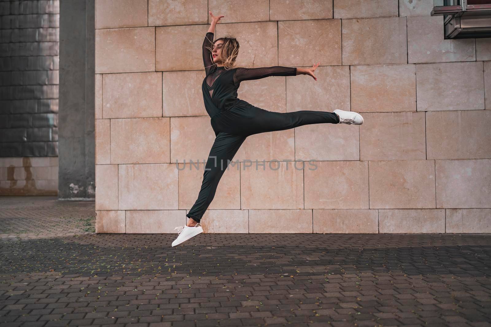 Young girl doing gymnastic jump on the street. by barcielaphoto