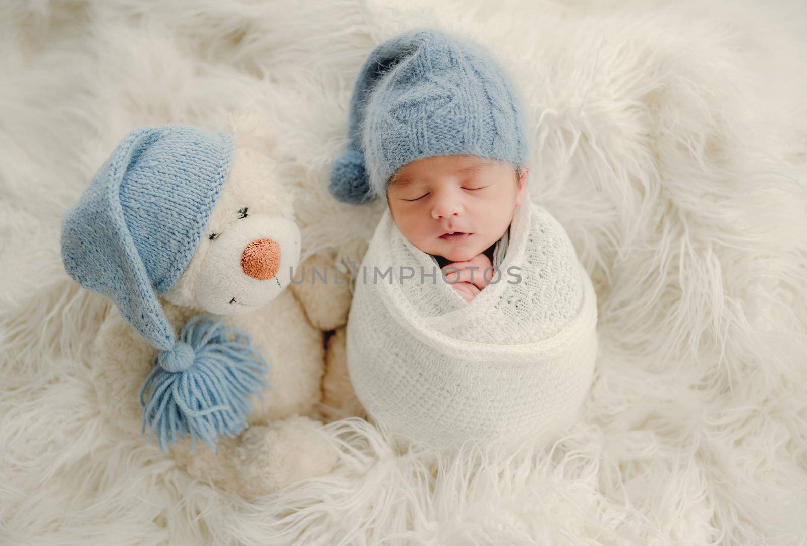Newborn baby boy with knitted snowman toy sleeping swaddled in fabric on white fur. Infant child kid Christmas and New Year holiday portrait