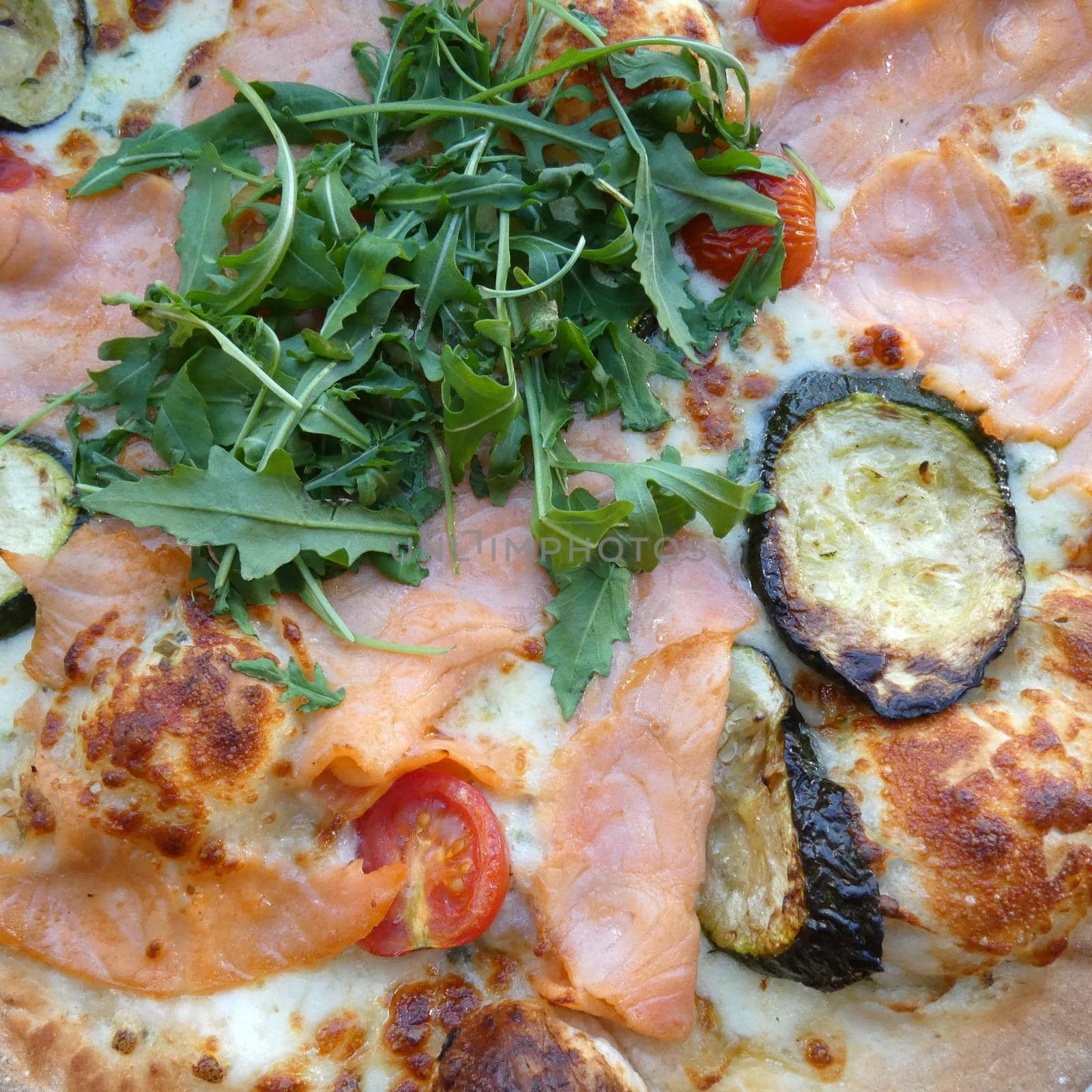 Pizza with fresh ingredients: salmon, tomatoes, aubergines, rucola salad,  cheese. Baked in a stone oven.