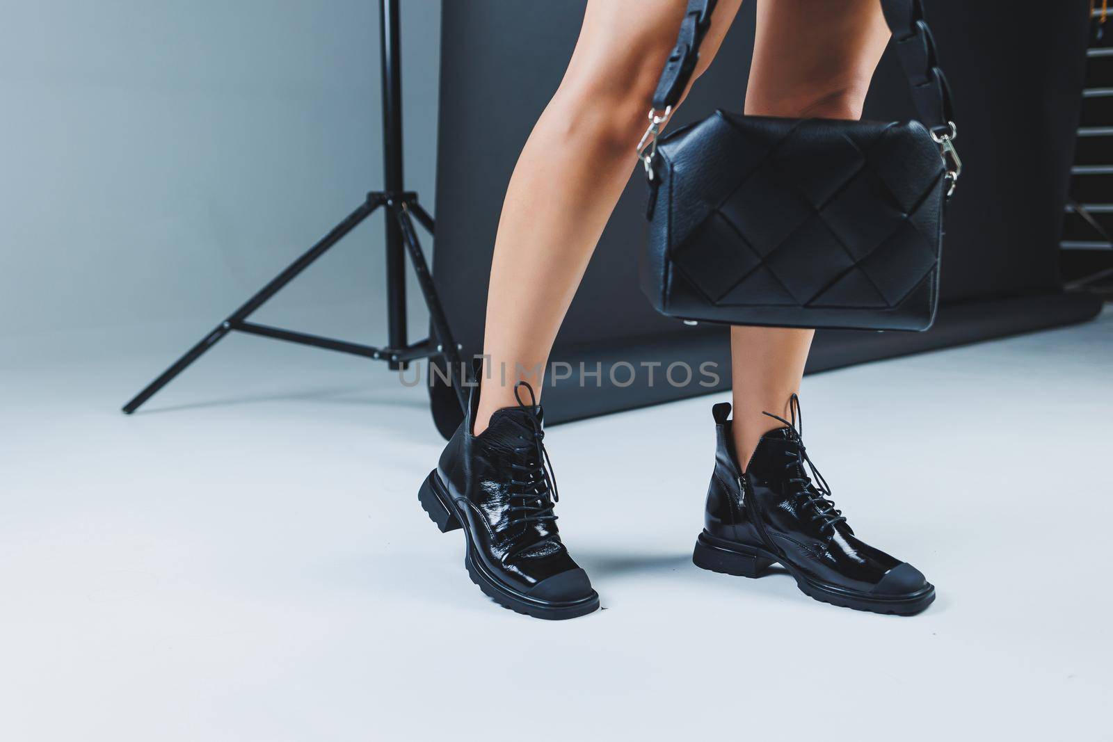 Close-up of female legs in black leather lace-up shoes. Black leather handbag in female hands. New autumn collection of women's leather shoes 2022