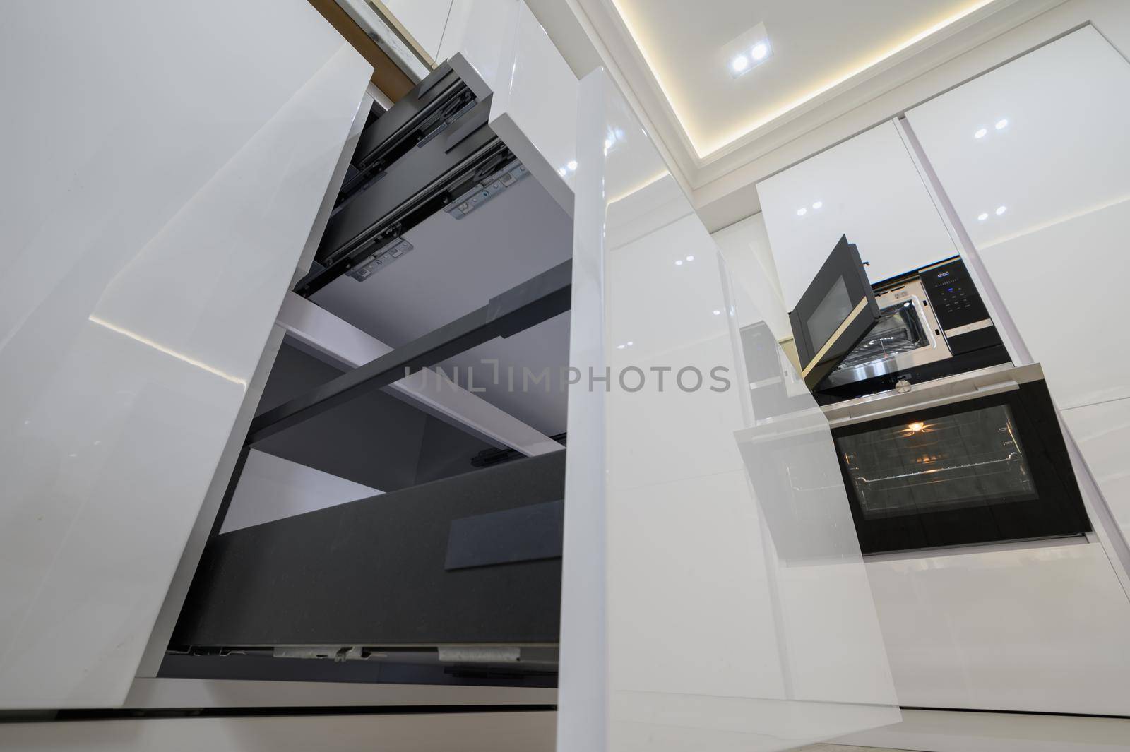 White modern kitchen with a stove, oven and microwave with open doors, drawers pulled out, high angle view