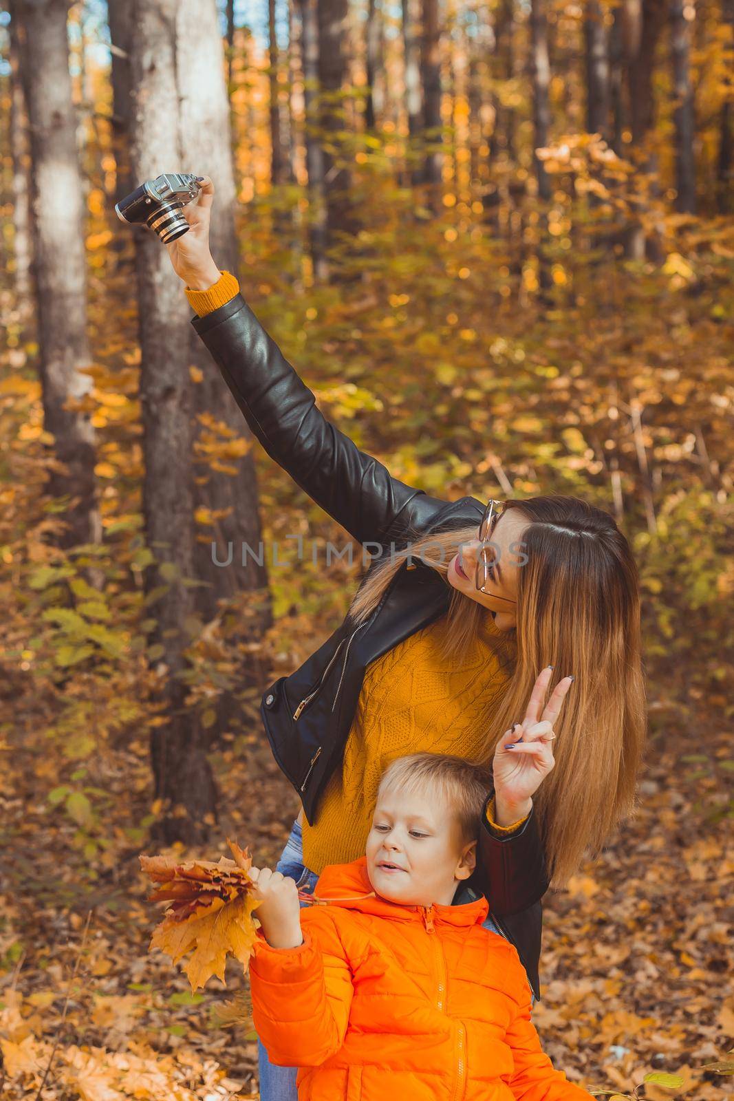Son and mother are taking selfie on camera in autumn park. Single parent, leisure and fall season concept. by Satura86