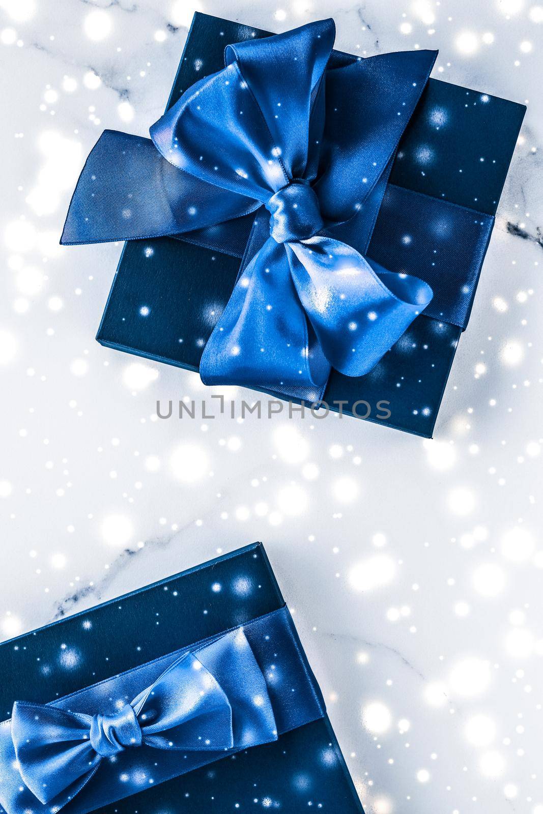 Branding, glamour and cold season concept - Winter holiday gift box with blue silk bow, snow glitter on marble background as Christmas and New Years presents for luxury beauty brand, flatlay design