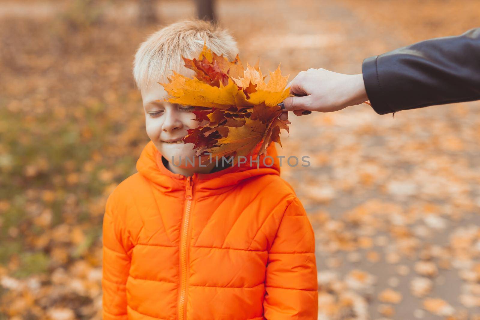 Portrait of happy child boy in orange jacket in autumn park. Fall season and children concept.