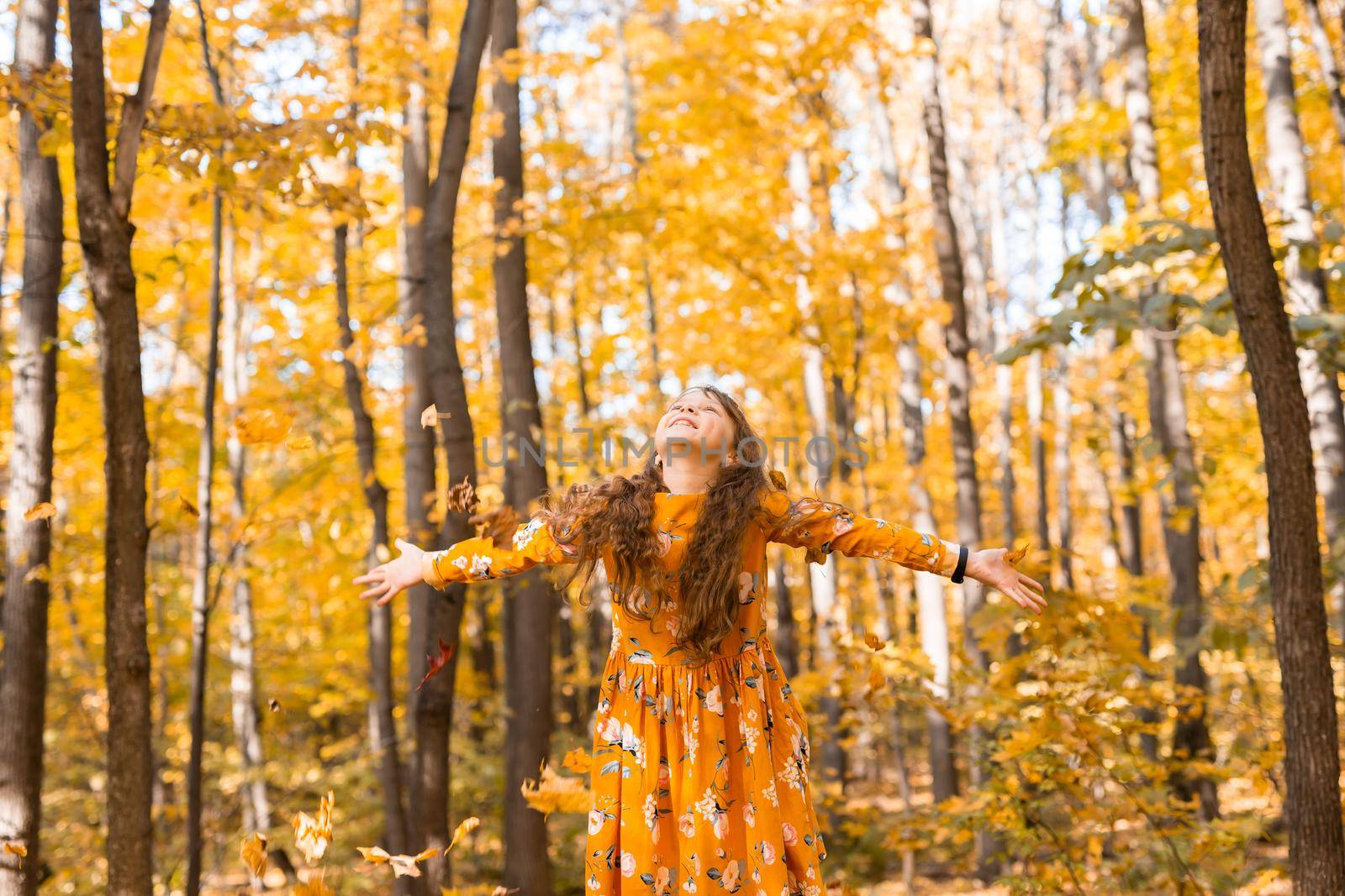 Child girl throwing fall leaves on autumn nature - fun, leisure and childhood