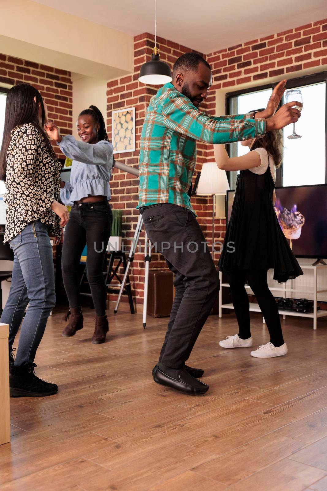 Young adult african american male vertical shot dancing at various ethnicities people party, gathering, reunion. Different nationalities friends group drinking wine, enjoying friendship.