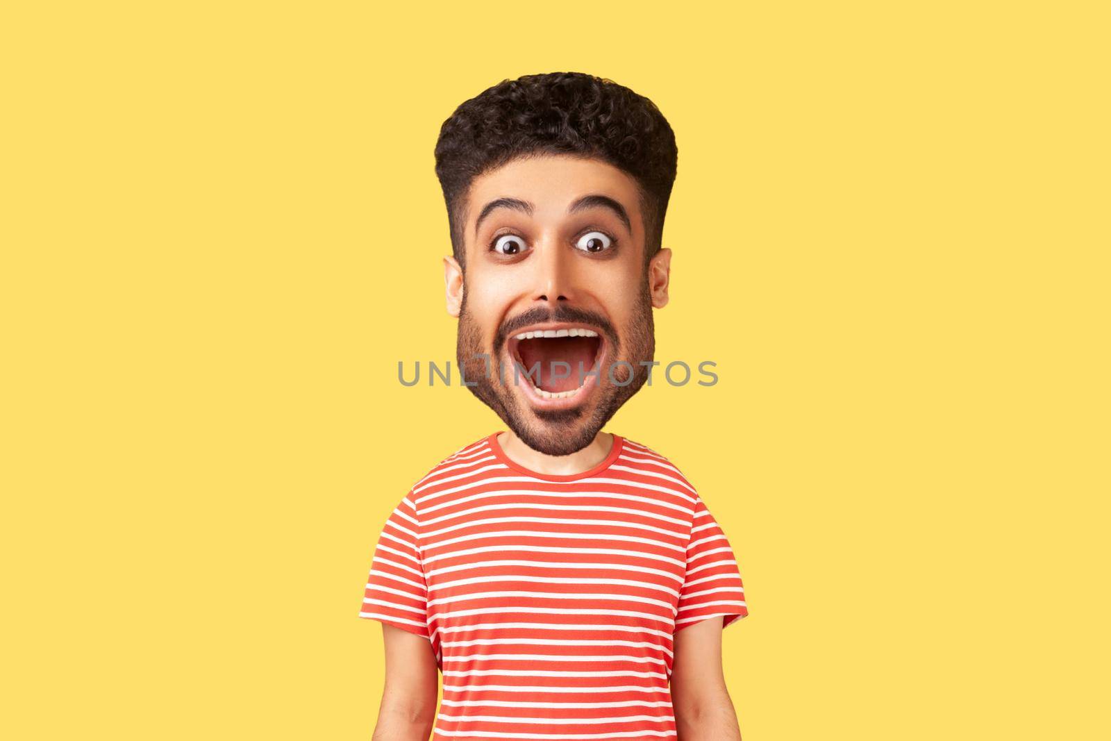 Caricature comic portrait of surprised funny young adult man looking at camera with open mouth and amazed big eyes, expressing astonishment. Indoor studio shot isolated on yellow background