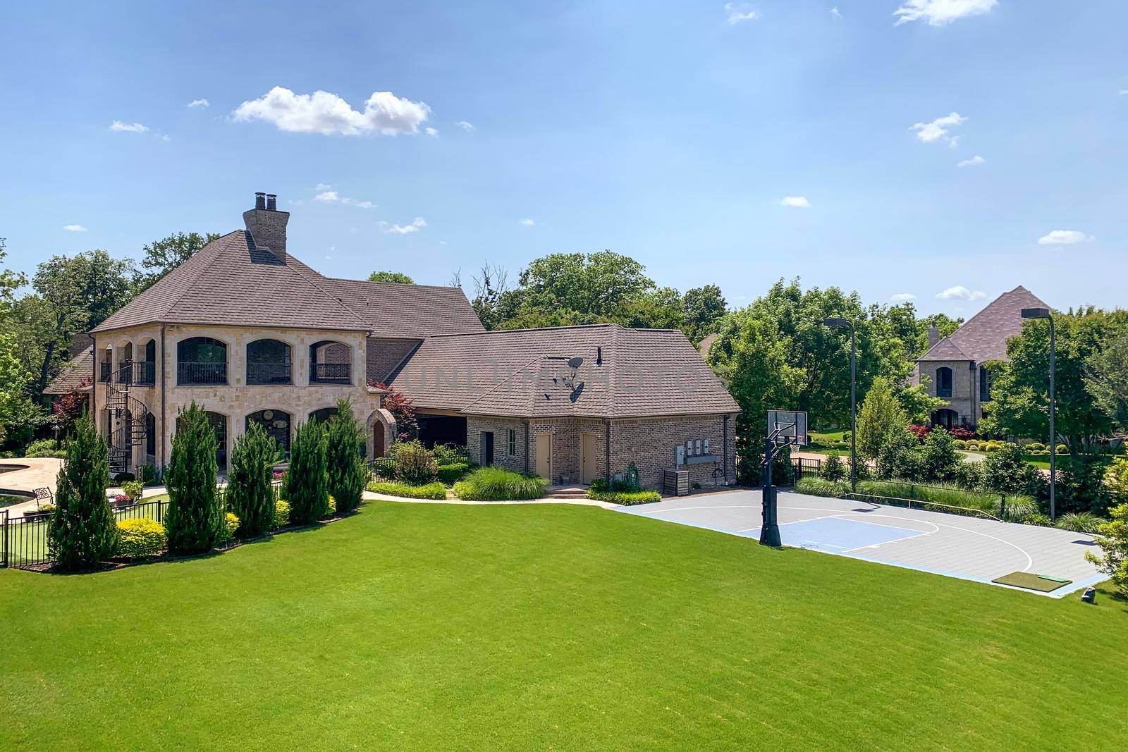 Outdoor shot of luxury house in suburban neighborhood with trees, bushes, lawn and basketball court on the backyard, blue sky background. Real estate concept.