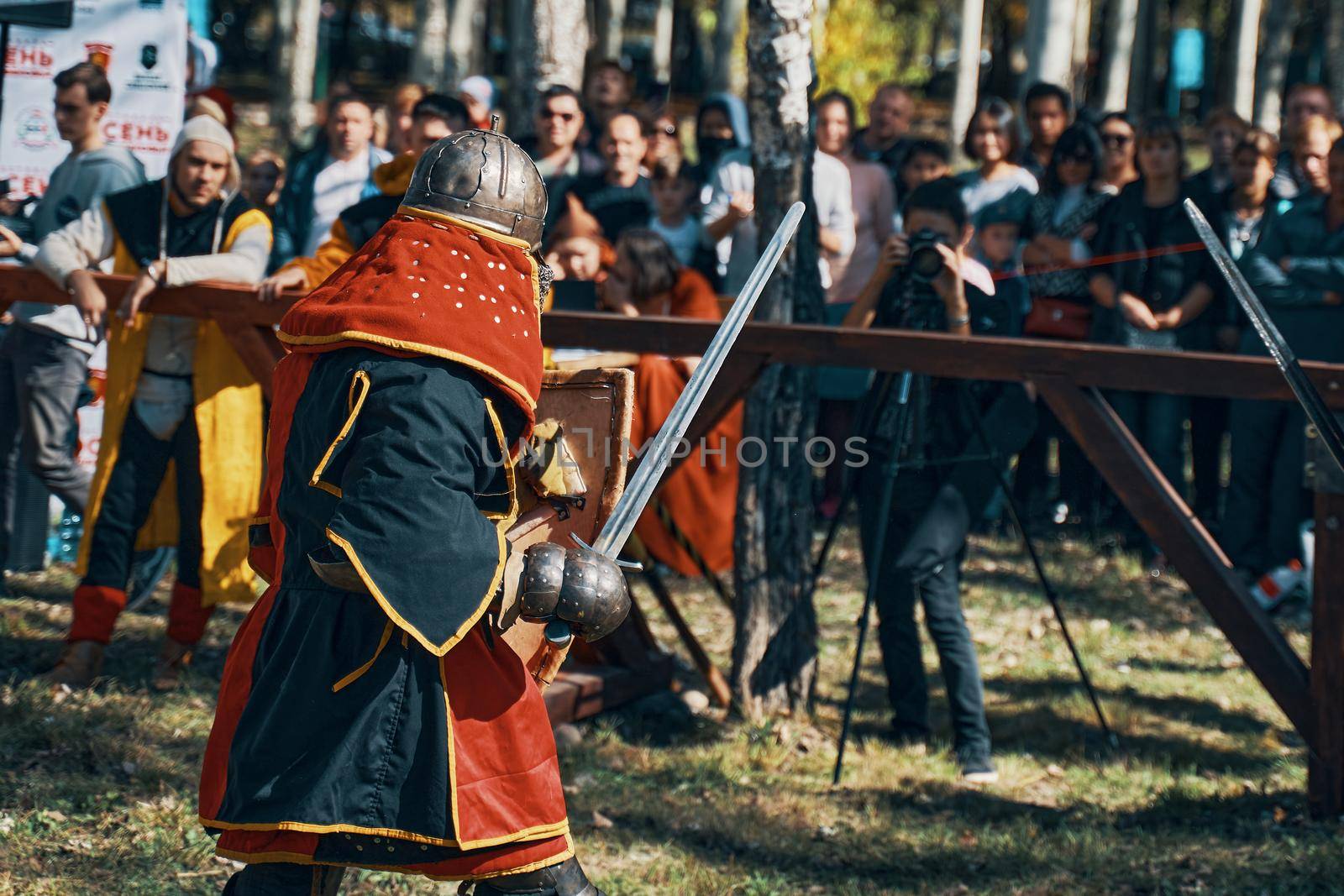 A warrior in red and black robes and a helmet. Festival of medieval culture. Imitation of jousting tournaments. Arena with spectators. Bishkek, Kyrgyzstan - October 13, 2019