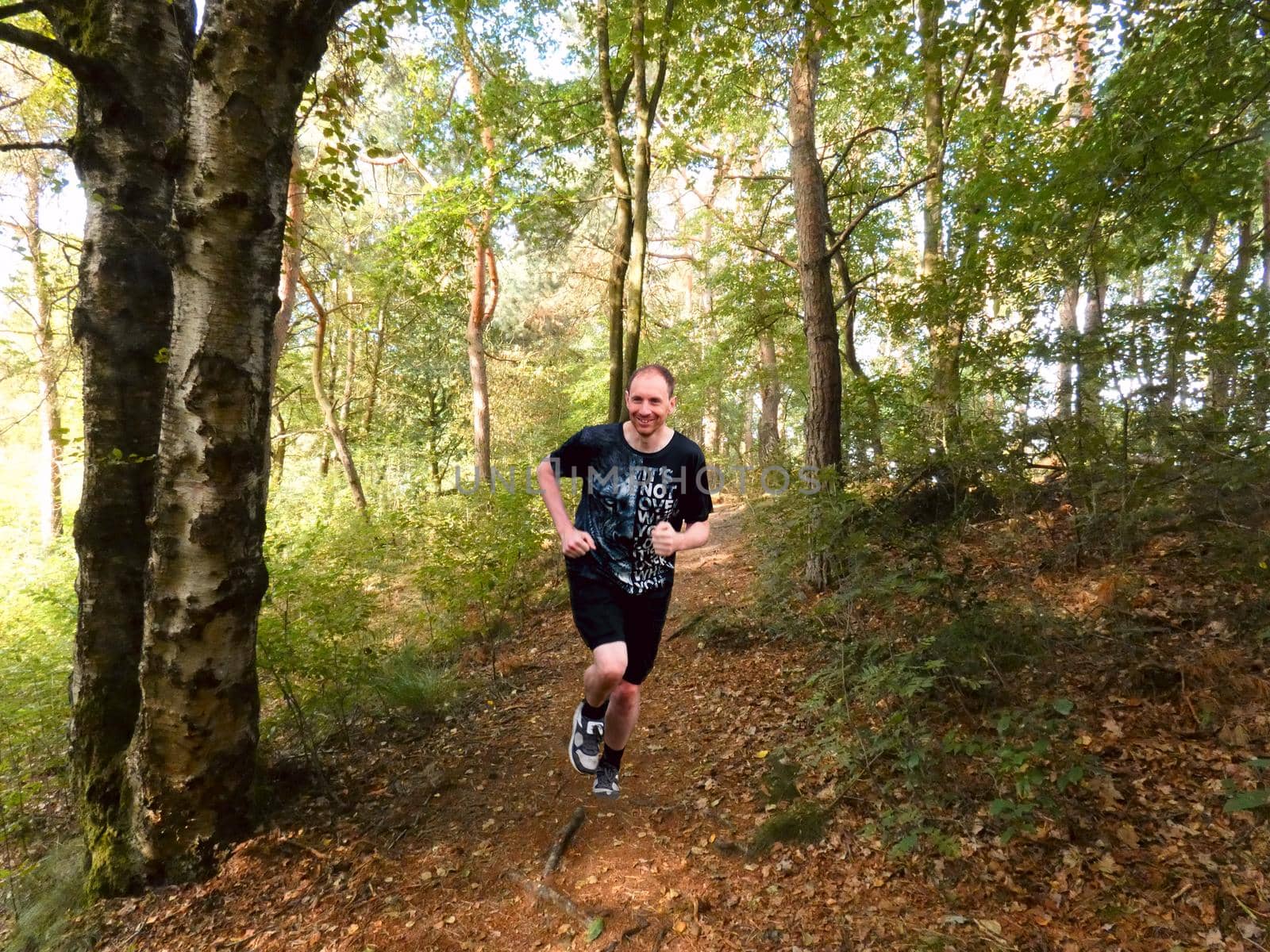 A man with t-shirt and shorts is running in the forest. He looks happy