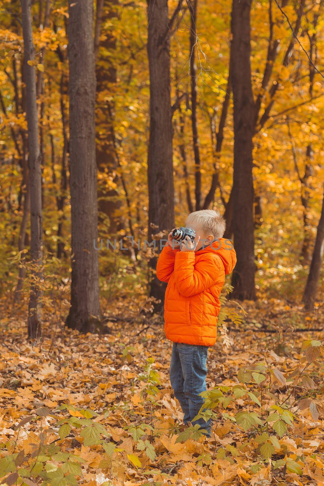 Boy with retro camera taking pictures outdoor in autumn nature. Leisure and photographers concept.