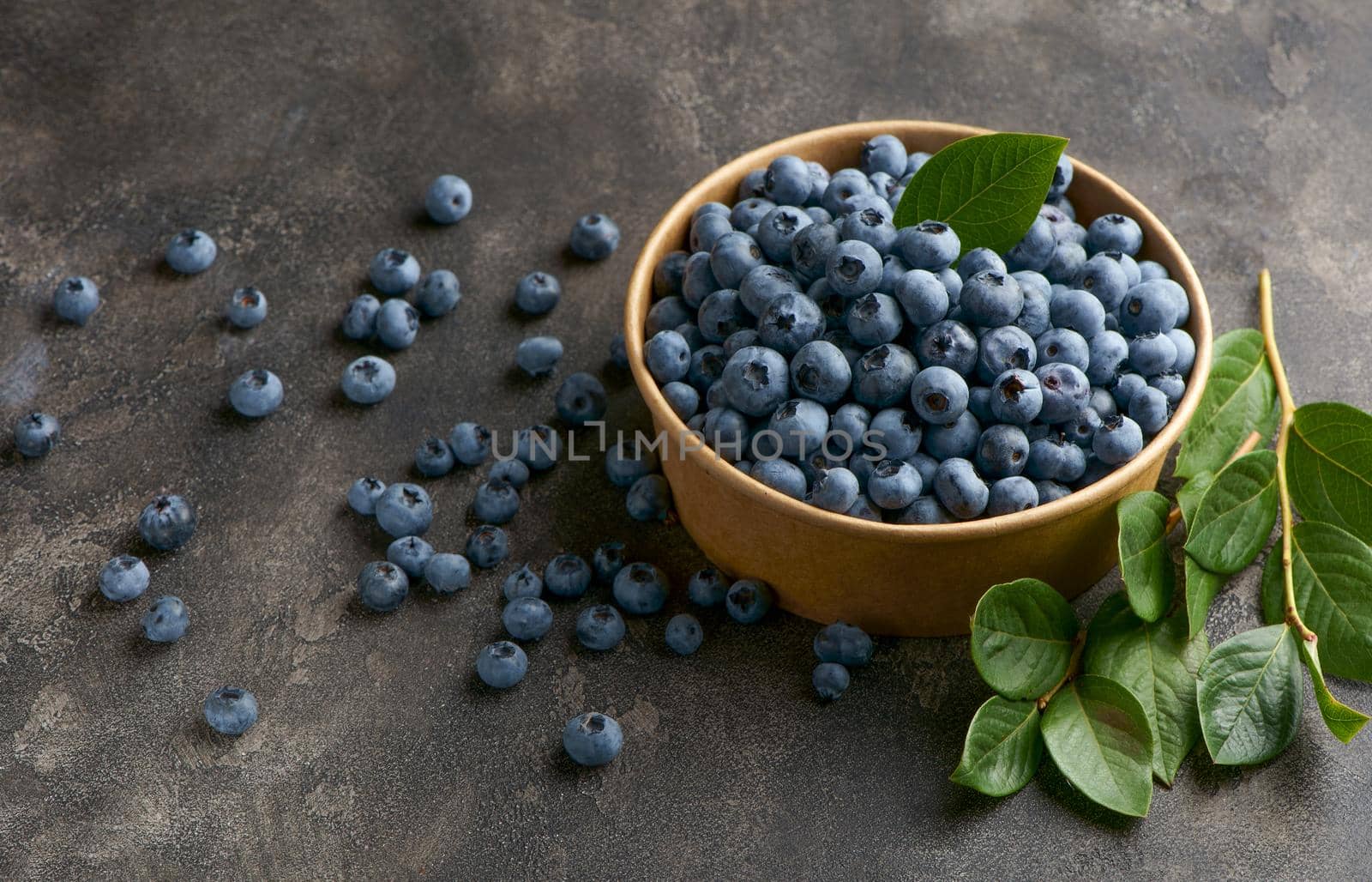 Freshly picked blueberries in a bowl. Juicy and fresh blueberries with green leaves on a rustic table. Blueberries on a wooden background. Blueberries antioxidant.